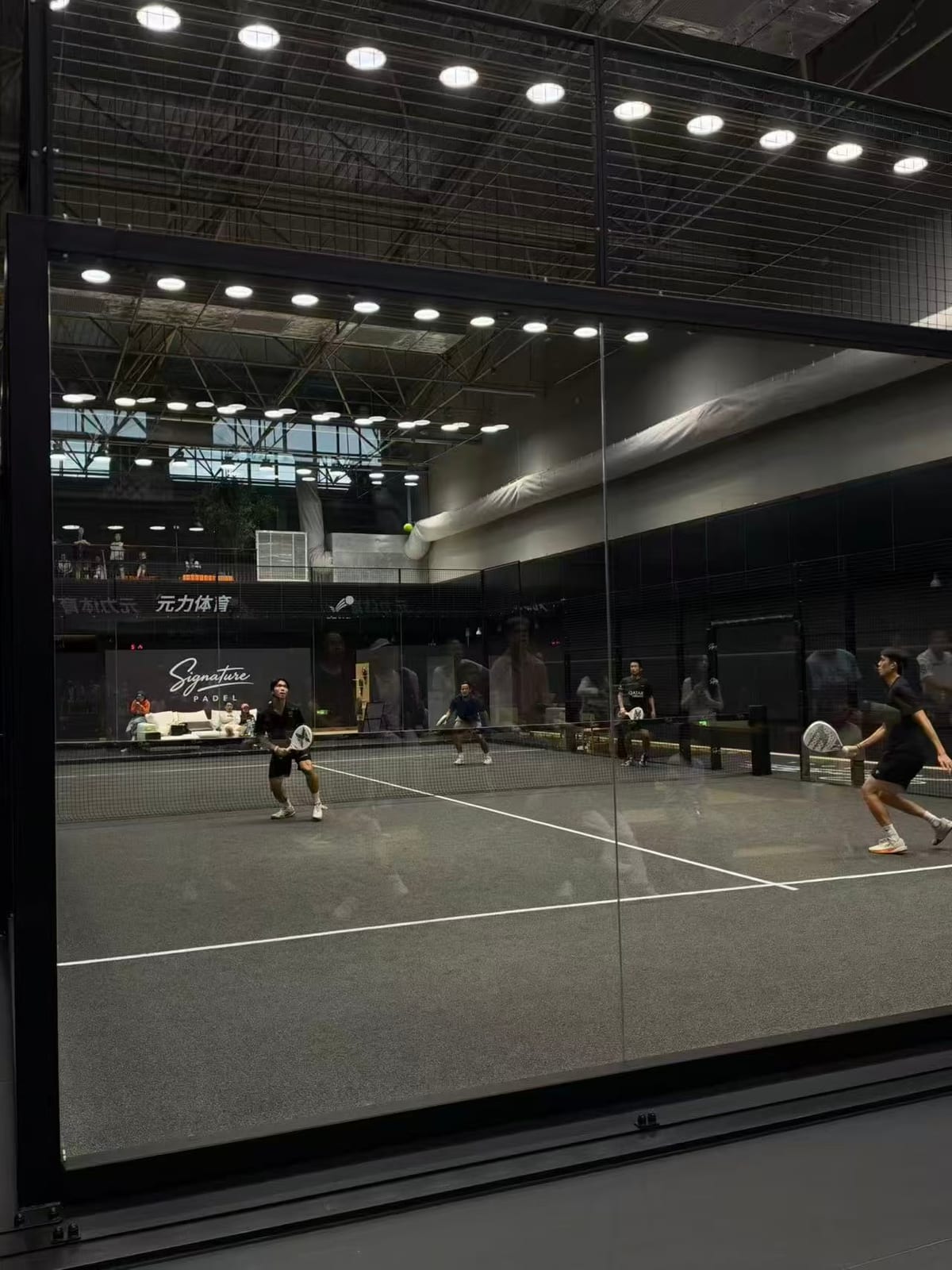 Four players mid-rally on a glass padel court at Signature Padel in Beijing